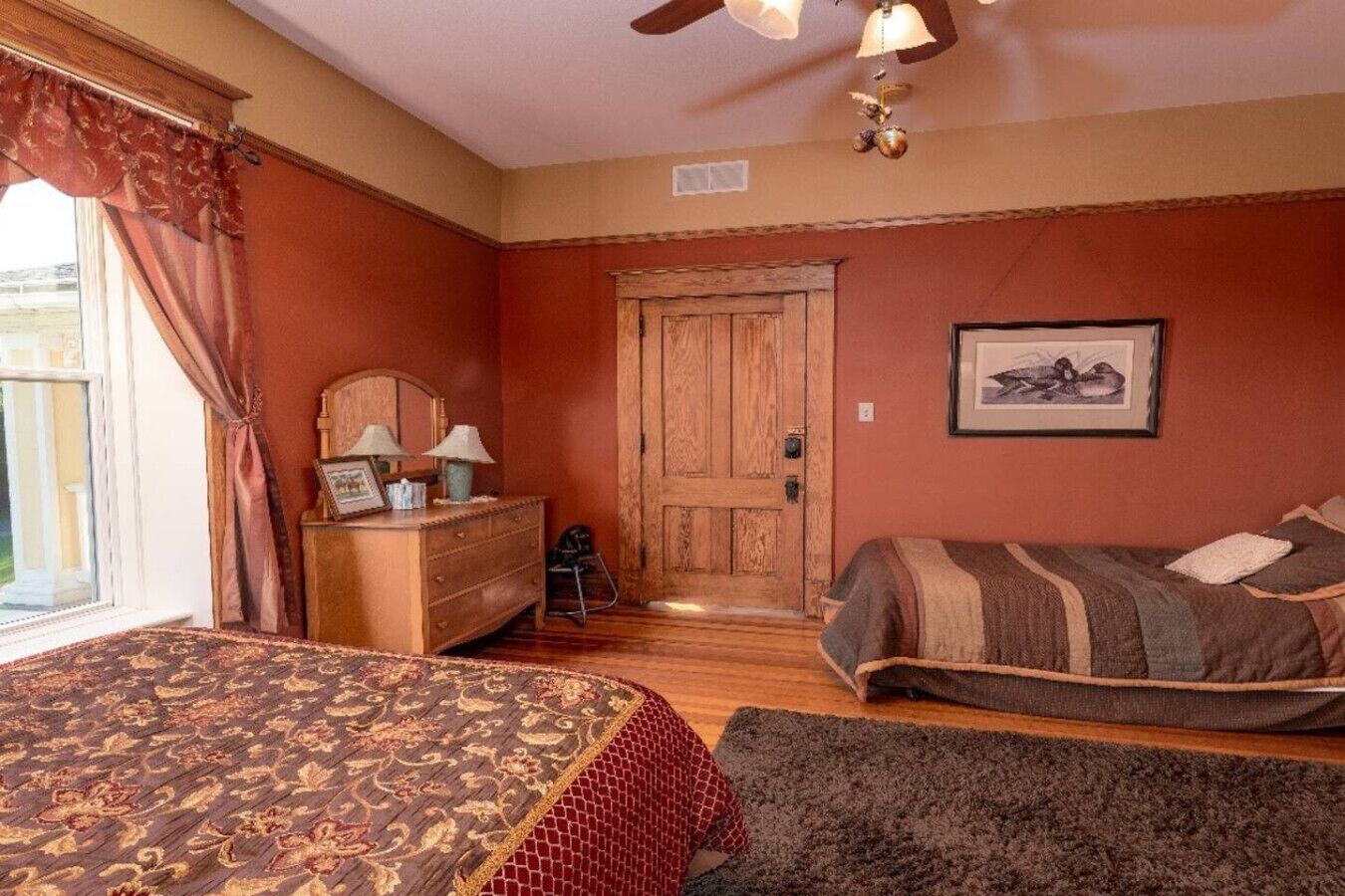 A bedroom with two beds, a wooden dresser, a chair, and a door.