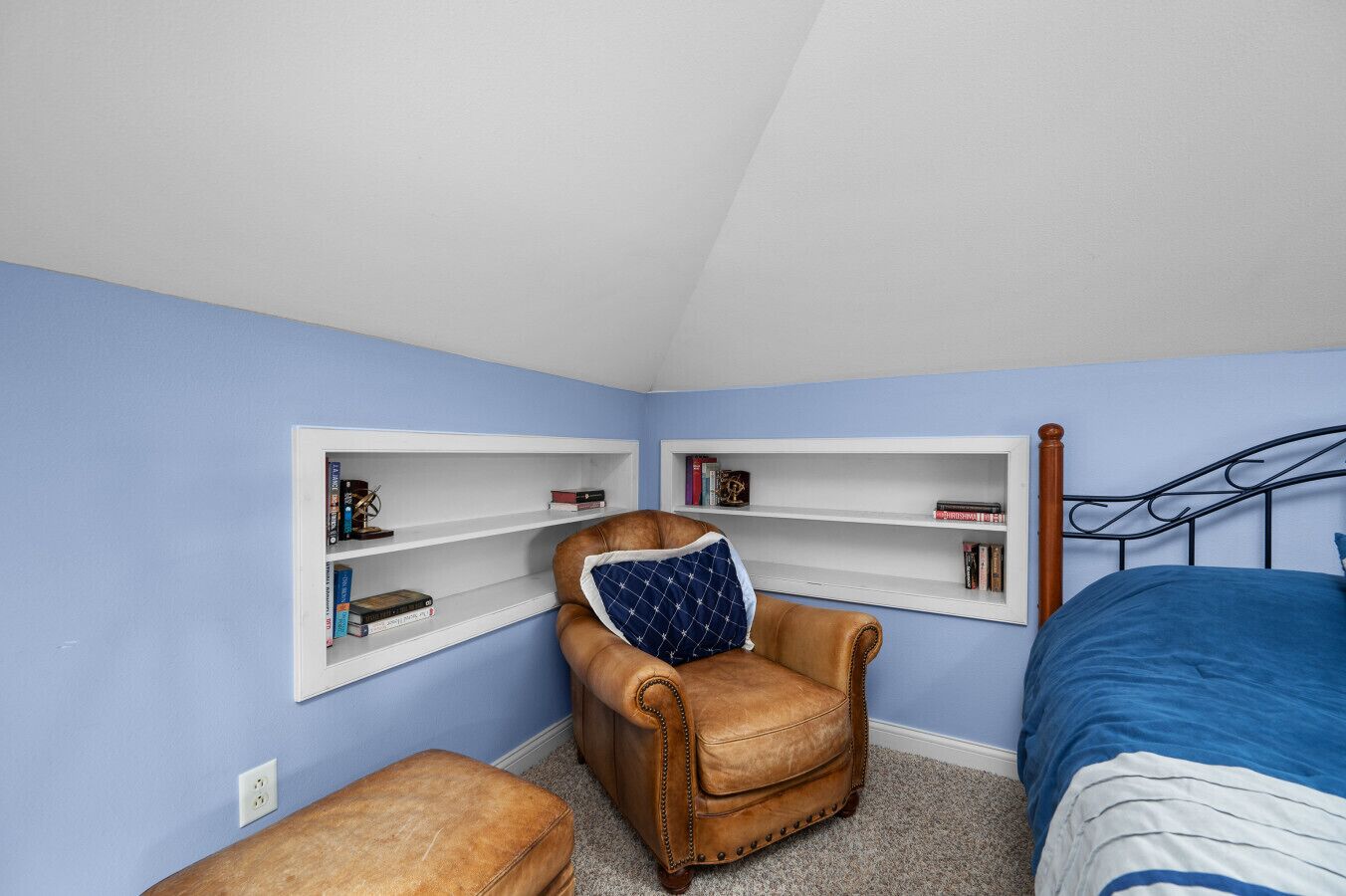 Une chambre avec un lit simple, une chaise, une petite table et deux étagères adossées au mur.