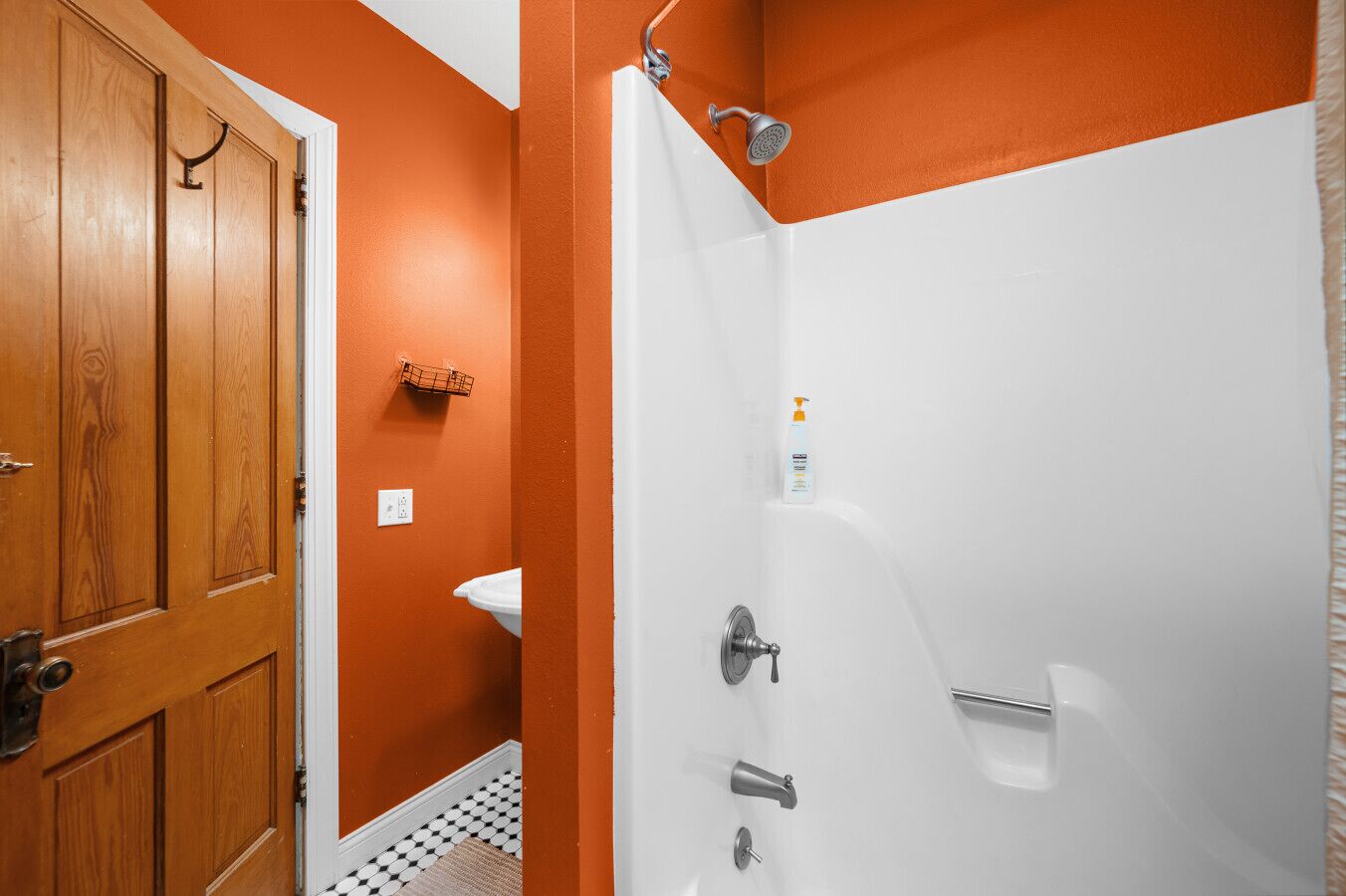 A bathroom with a wooden door, a white sink, and a shower with a handheld showerhead.