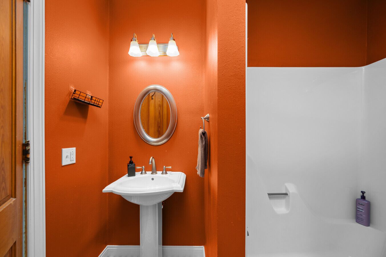 Une salle de bain avec un mur orange, un lavabo blanc, un miroir et un porte-serviettes.