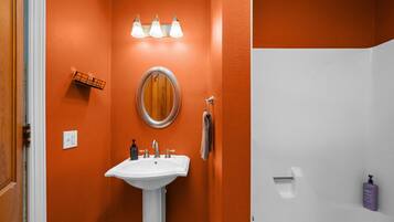 Une salle de bain avec un mur orange, un lavabo blanc, un miroir et un porte-serviettes.