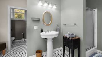 A bathroom with a white pedestal sink, a round mirror with a gold frame, and a towel rack.
