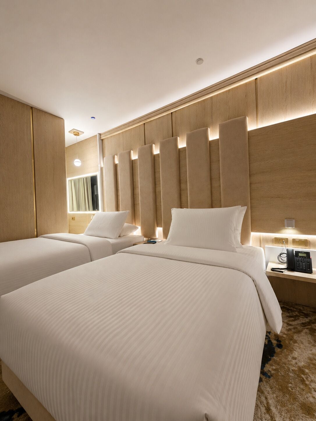 Une chambre d’hôtel avec deux lits, une table de chevet avec un téléphone et un luminaire fixé au mur.