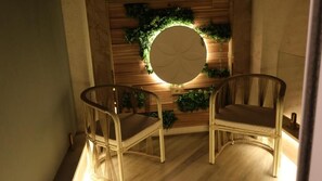 Une pièce avec deux fauteuils en osier, un miroir rond et un mur en bois orné de plantes vertes.