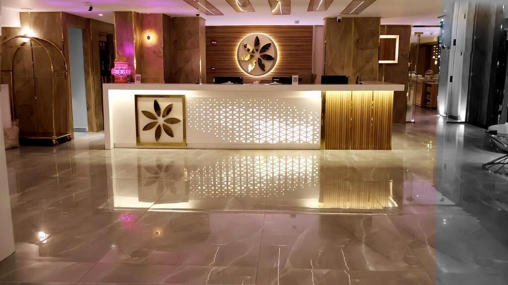 Un área de recepción con diseño moderno, que incluye un mostrador de recepción, una pared decorativa y un espejo grande.