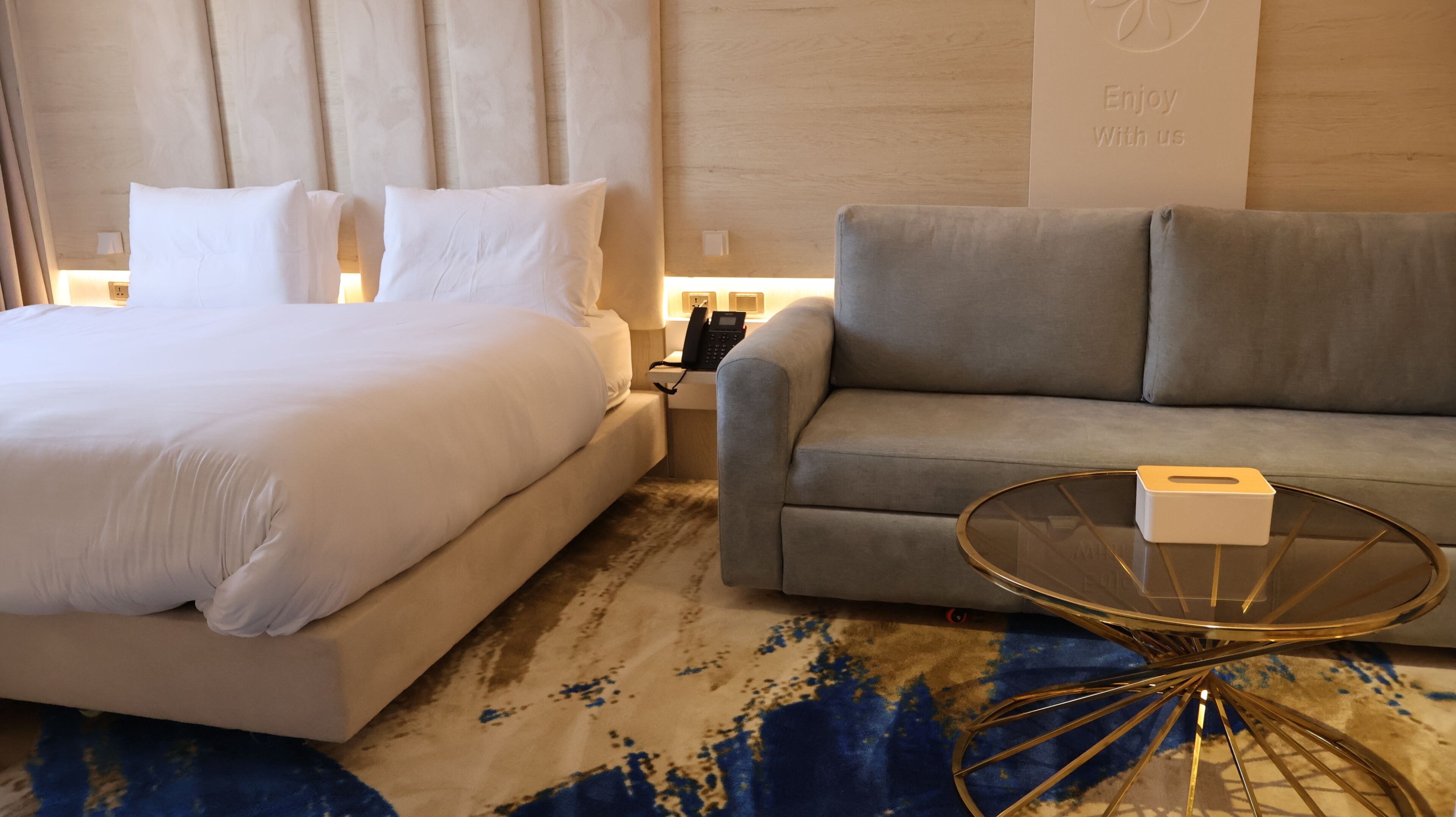 Una habitación de hotel con una cama, un sofá, una mesita de vidrio y una pared con un logotipo.