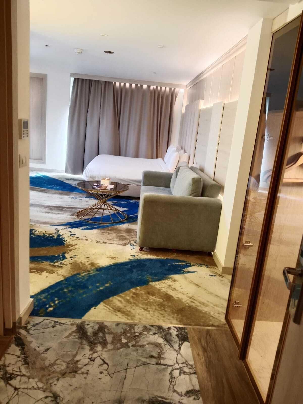 Ein Hotelzimmer mit einem Bett, einem grauen Sessel, einem Couchtisch und einem gemusterten Teppich.