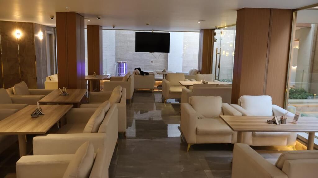 Rebedor modern d'hotel amb diverses zones d'estar, una televisió amb pantalla plana i grans finestres.