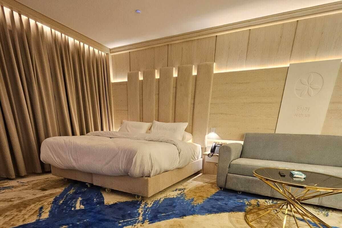 Una habitación de hotel moderna con una cama grande, un sofá, una mesa de centro de vidrio y una alfombra estampada.
