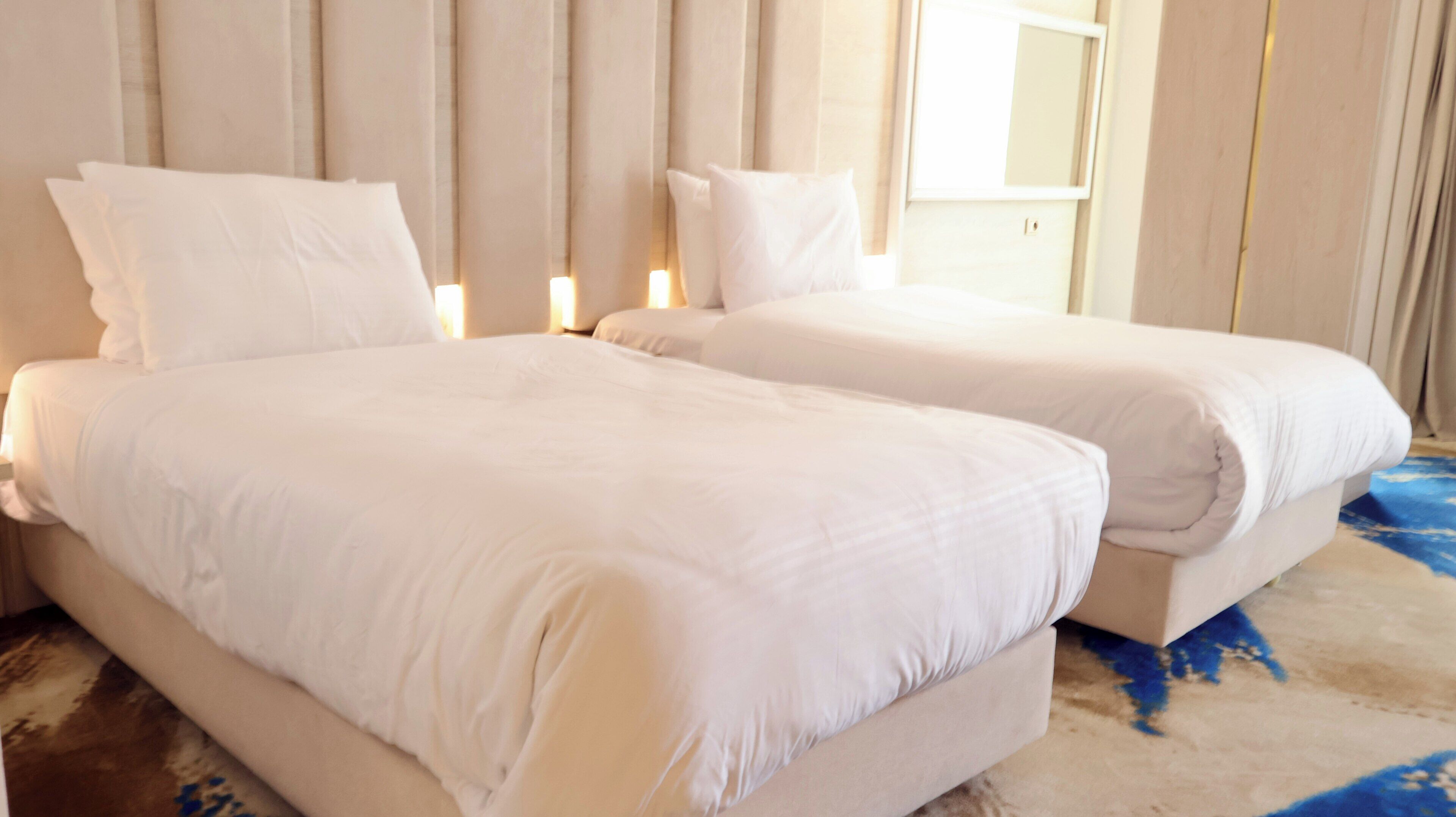 A hotel room with two beds, a large window, and a light-colored rug.