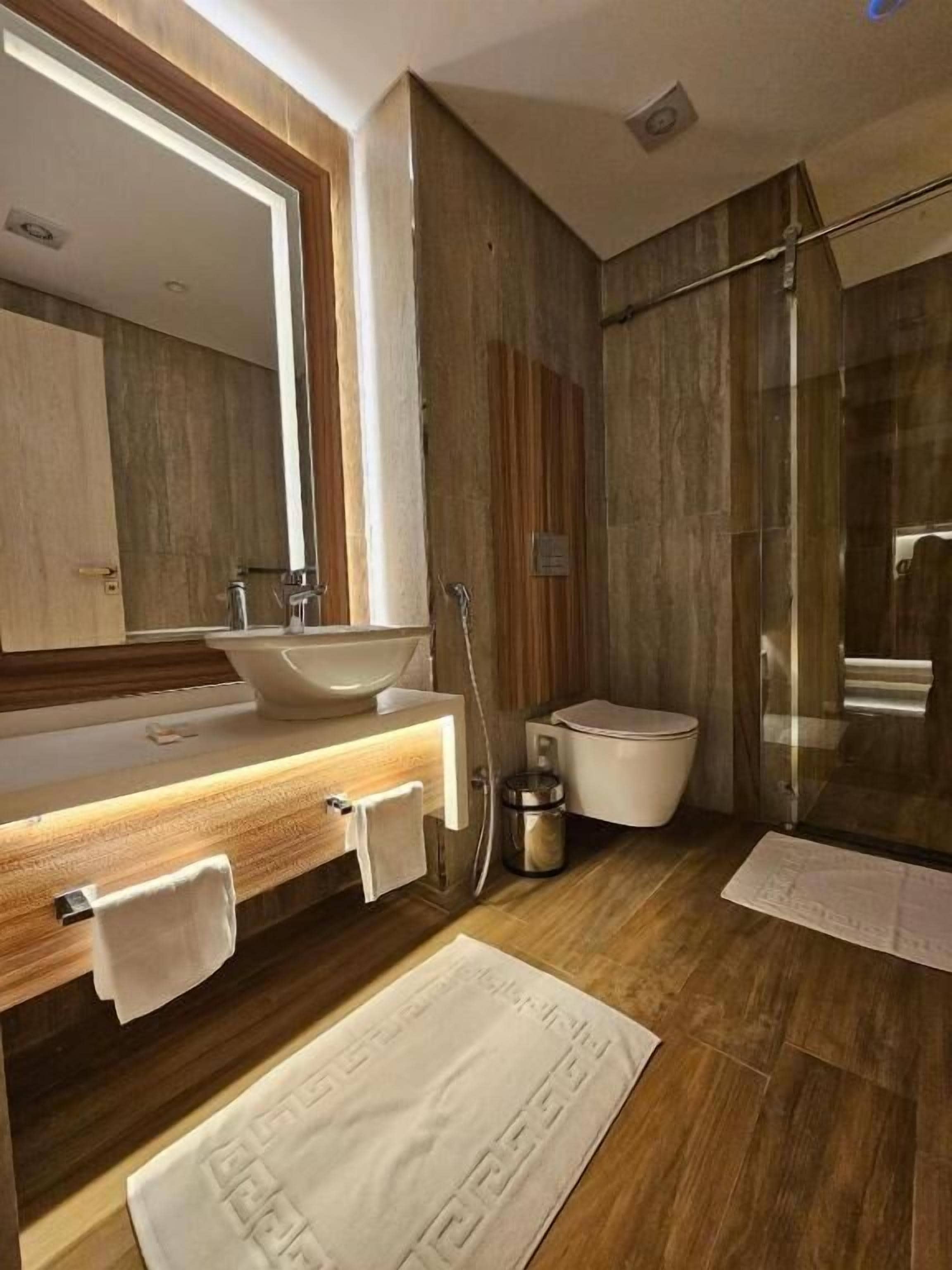 Un baño moderno con un espejo grande, tocador de madera, lavabo blanco y cabina de ducha de vidrio.