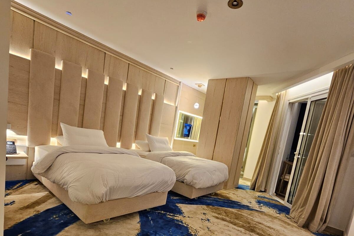A modern hotel room with a large bed, a separate sofa, a large window, and a view of the city.