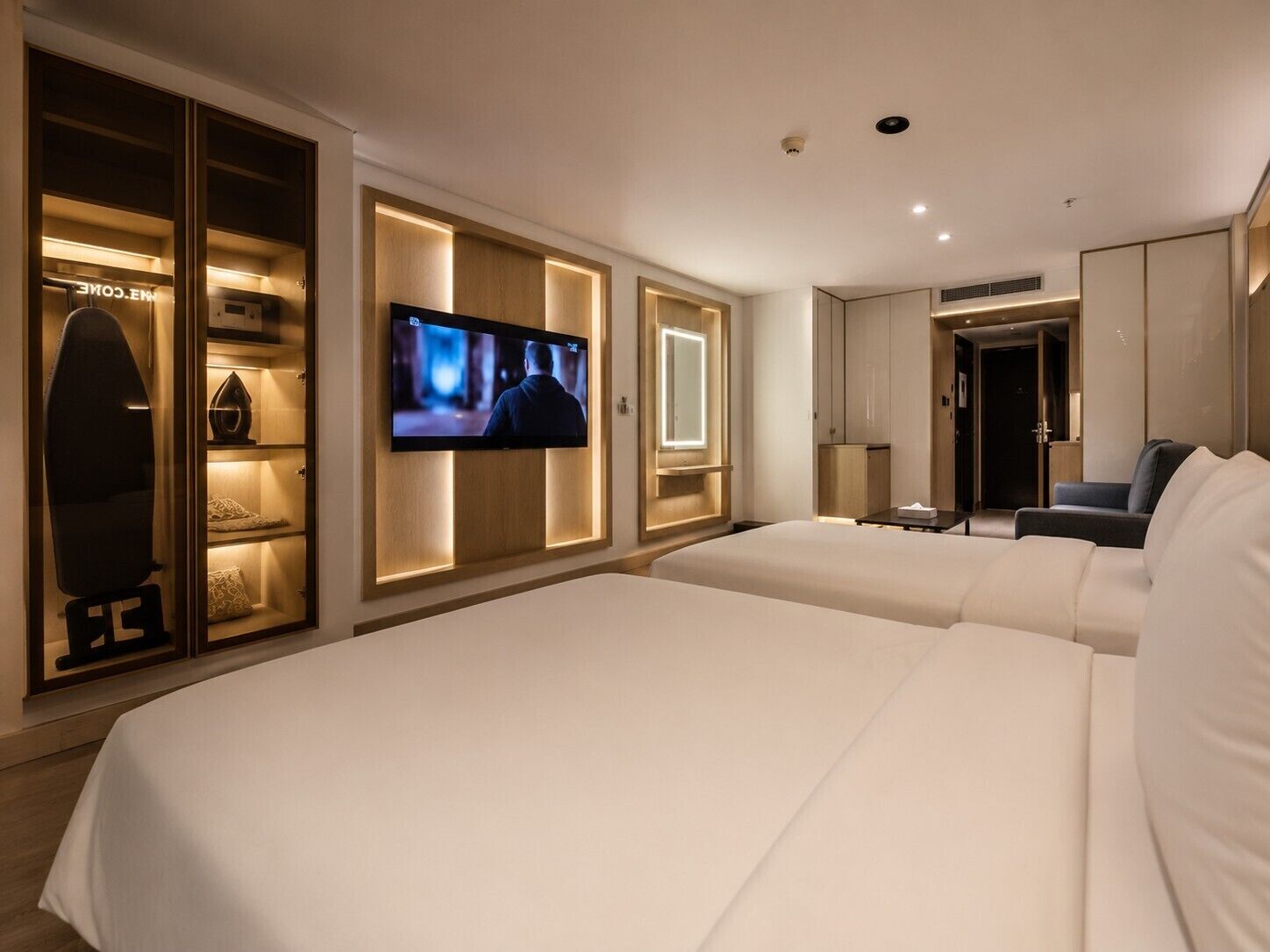 Habitación de hotel con dos camas, televisor montado en la pared, armario y zona de estar.