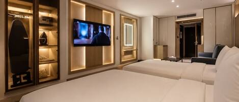 A hotel room with two beds, a TV mounted on the wall, a wardrobe, and a seating area.