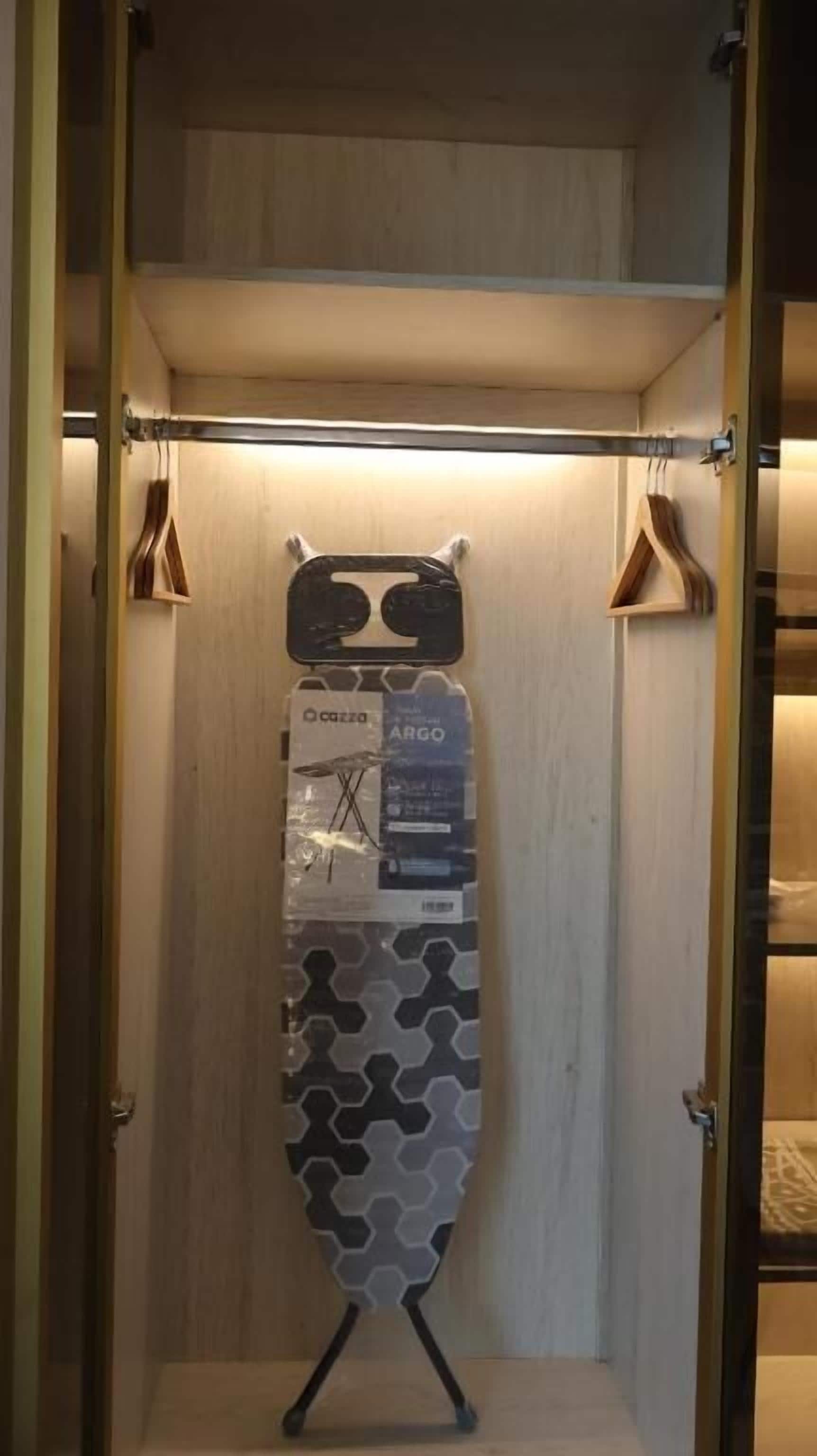 A room with a wooden door, a hanging coat rack, and a wall-mounted ironing board.