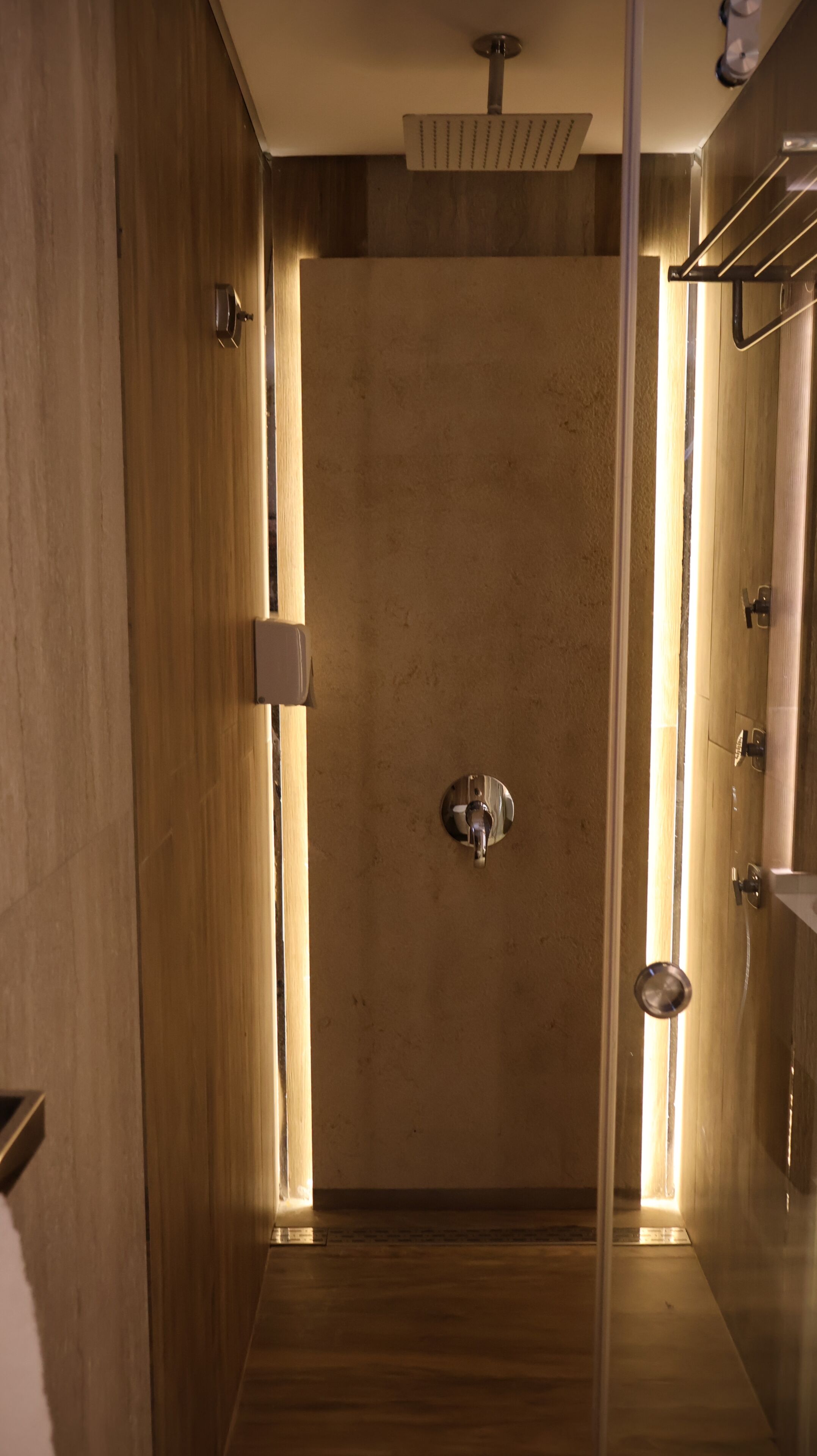 A modern bathroom with a shower, a towel rack, and a light fixture.