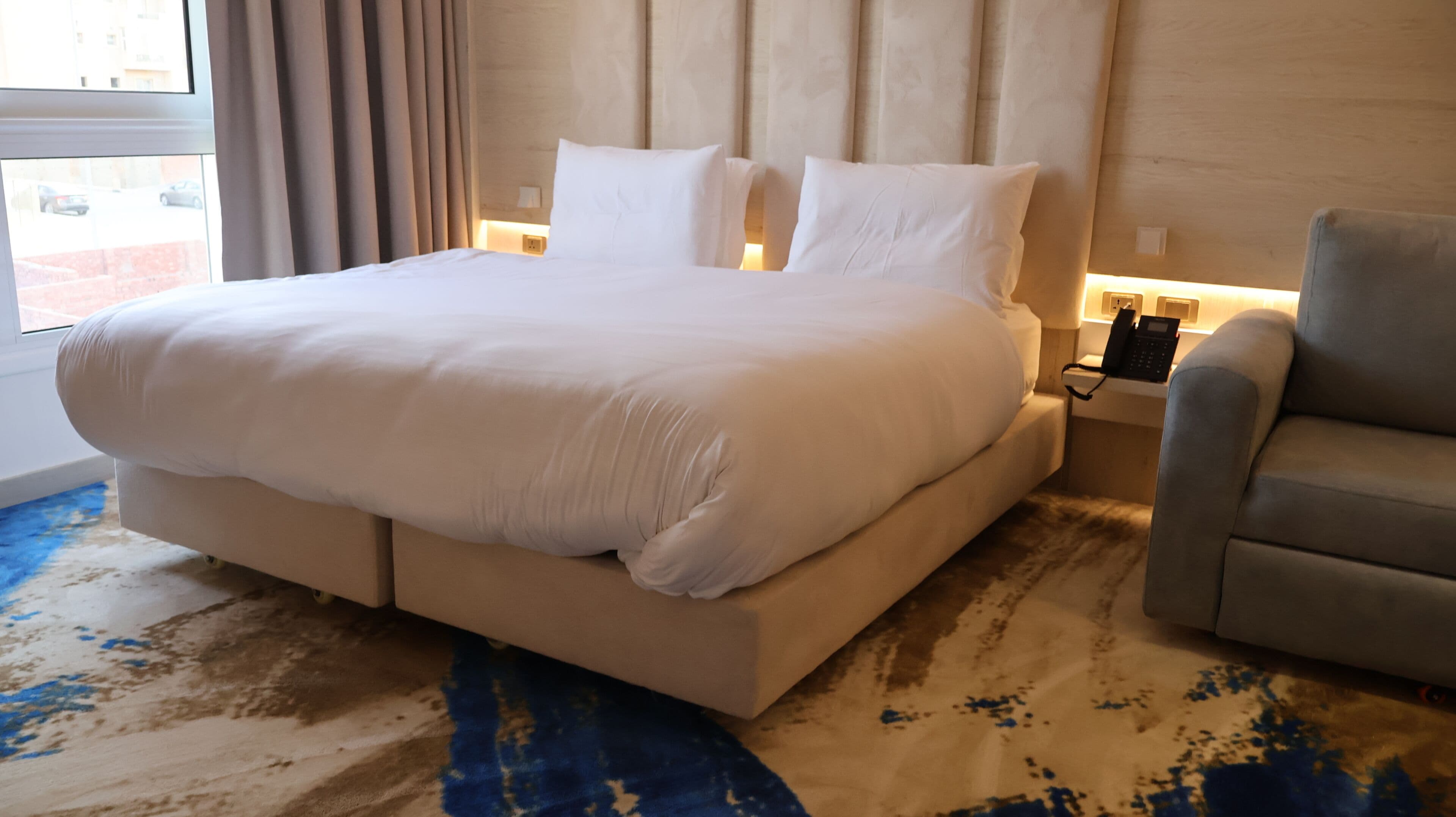 Une chambre d’hôtel avec un grand lit, une table de chevet avec un téléphone et une chaise.