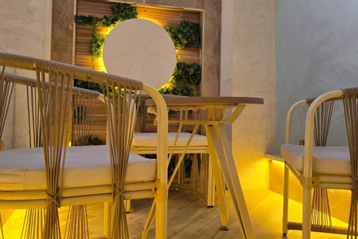 Un espacio moderno al aire libre con sillas de mimbre y una mesa, rodeado por un muro decorativo con plantas y un accesorio de iluminación circular.