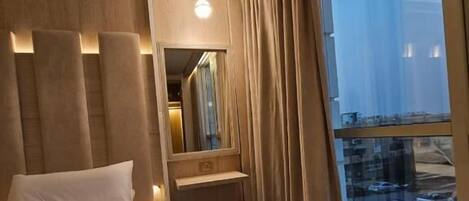 Een hotelkamer met een groot bed, een nachtkastje, een spiegel en een raam met uitzicht op een parkeerplaats.