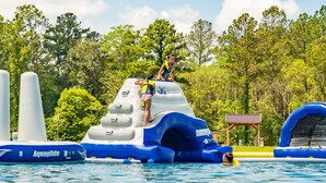 Un tobogán acuático inflable con diseño azul y blanco, una persona escalándolo y otra al pie.