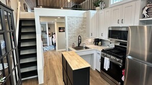 A modern kitchen with a wooden ceiling, a central island, stainless steel appliances, and a staircase leading to an upper level.