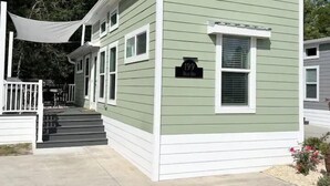 Une maison à deux étages, avec une façade verte et des éléments décoratifs blancs, un porche à l’avant et une plaque indiquant l’adresse.