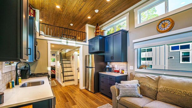 A modern kitchen with wooden ceiling, a dining area with a sofa, and a staircase leading to an upper level.