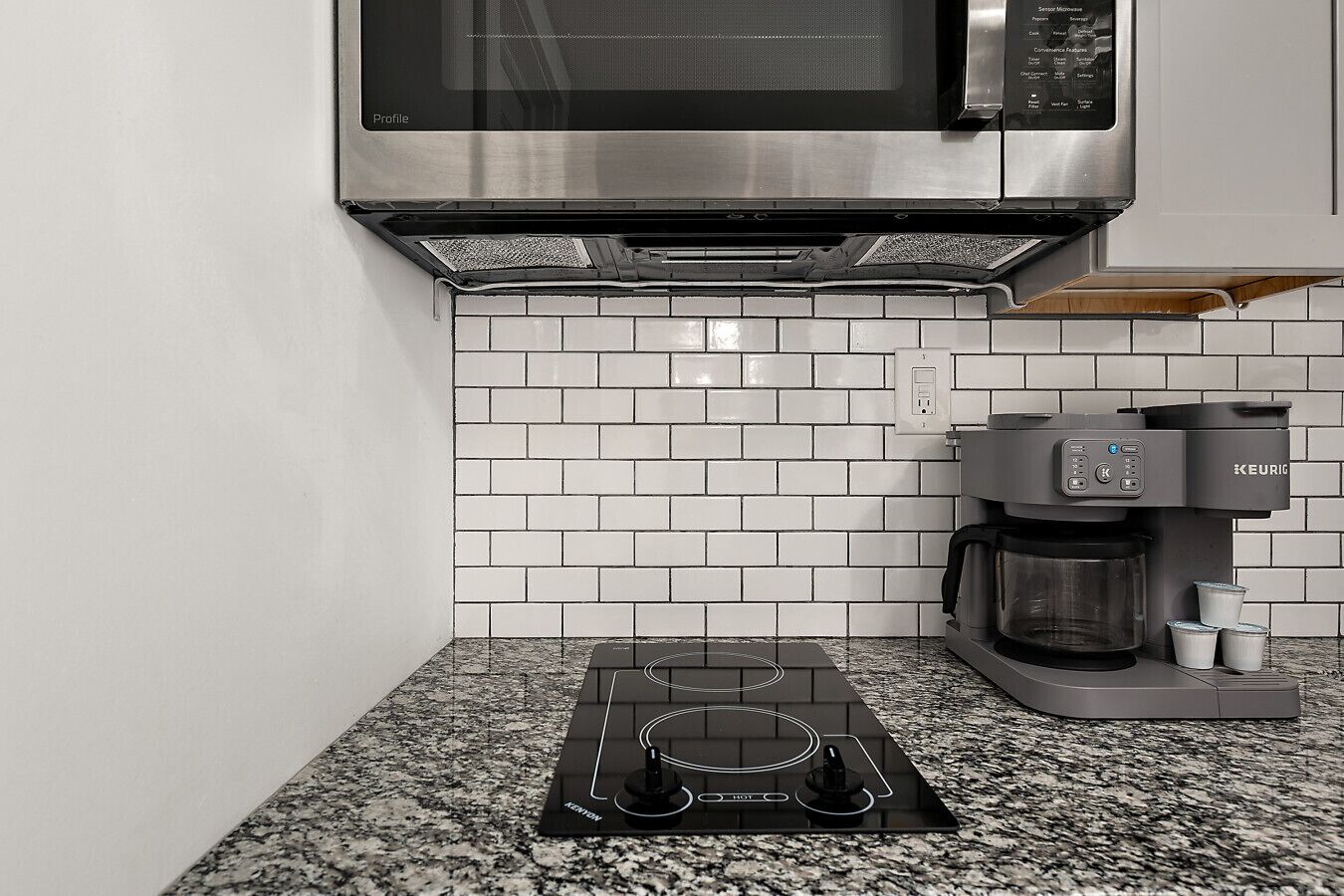 A kitchen with a stainless steel microwave, a Keurig coffee maker, and a black induction cooktop.