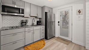 A modern kitchen with white cabinets, a stainless steel refrigerator, a microwave, and a coffee maker. - Surf 3 - Steps to beach and OC Boardwalk (Ocean City)