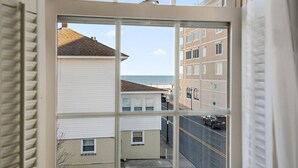 A view through a window of a building with a street and a beach in the background. - Surf 1 - Steps to the beach and boardwalk (Ocean City)