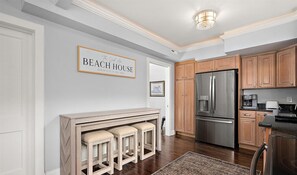 A kitchen with wooden cabinets, a stainless steel refrigerator, and a bar area with stools. - Surf 1 - Steps to the beach and boardwalk (Ocean City)