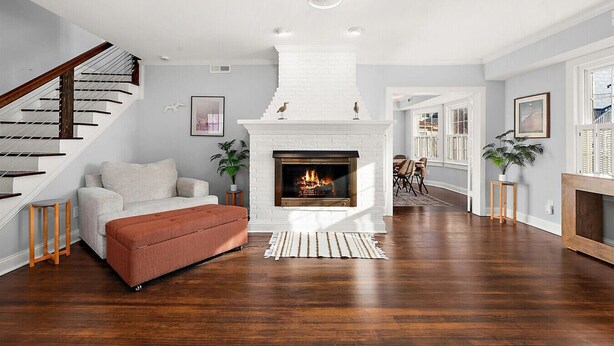 A spacious living room with a white fireplace, a wooden staircase, and a dining area with a view. - Surf 1 - Steps to the beach and boardwalk (Ocean City)
