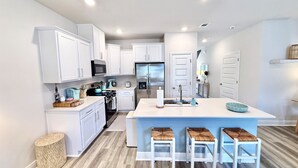 Une cuisine moderne avec des meubles blancs, un îlot central doté de tabourets, des appareils en acier inoxydable et un plancher en bois.