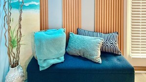 Une pièce avec un canapé bleu, des stores à rayures verticales et une décoration murale sur le thème de la plage.