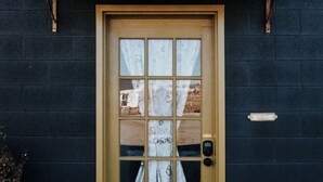 A yellow door with a grid pattern, a small window, and a bell above it.