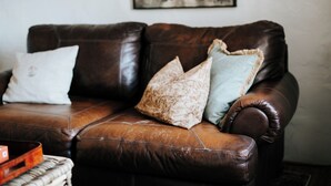 A brown leather sofa with three cushions in a living room.