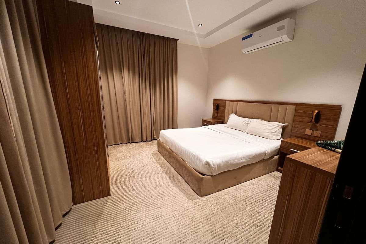 Een hotelkamer met een groot bed, een houten hoofdeinde, een nachtkastje, een bureau en een airconditioner aan de muur.