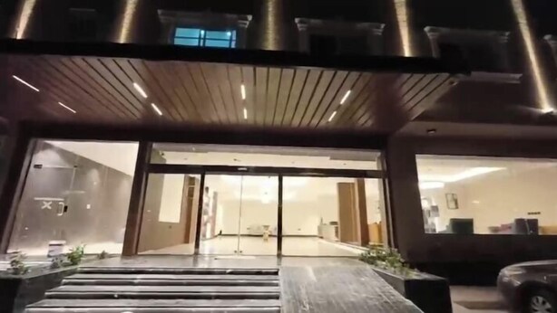 Une entrée moderne, avec un auvent en bois, des portes en verre et une voiture garée à l’extérieur.