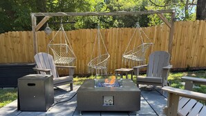 Een terras met Adirondack-stoelen, een vuurkuil en een vuilnisbak.
