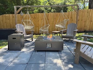 A patio with Adirondack chairs, a fire pit, and a trash can. - Modern High Point Retreat - Private Gym, Game Room, Fire Pit, Fenced Yard (High Point)