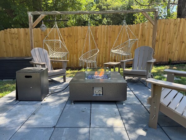 A patio with Adirondack chairs, a fire pit, and a trash can. - Modern High Point Retreat - Private Gym, Game Room, Fire Pit, Fenced Yard (High Point)