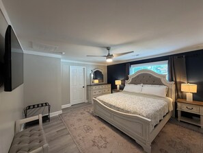 A bedroom with a bed, a ceiling fan, a TV mounted on the wall, and a window with curtains.