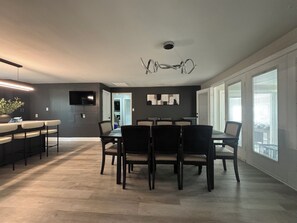 A modern kitchen with a dining area, a flat-screen TV mounted on the wall, and a ceiling light fixture. - Modern High Point Retreat - Private Gym, Game Room, Fire Pit, Fenced Yard (High Point)