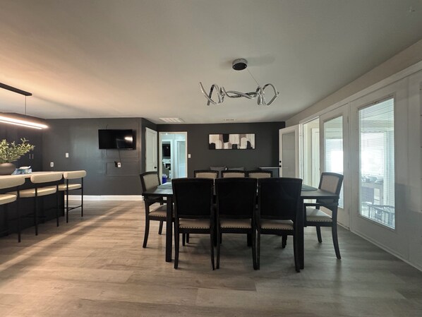 A modern kitchen with a dining area, a flat-screen TV mounted on the wall, and a ceiling light fixture. - 7 Min to HPU • Private Gym • Game Room • Fire Pit • Sleeps 9 (High Point)