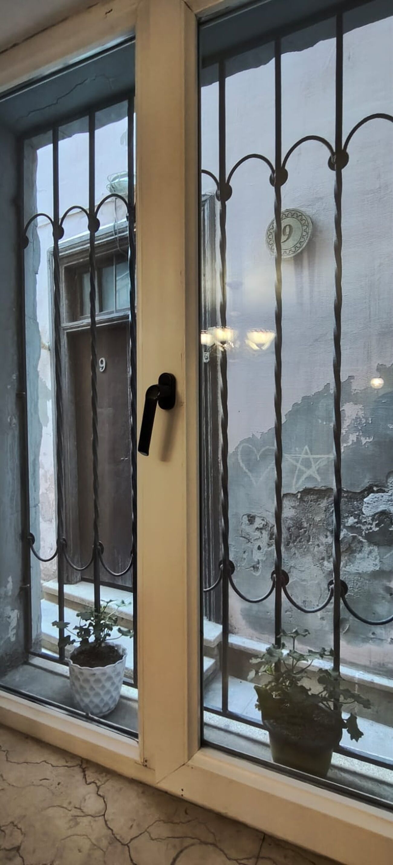 Et vindue med metalgitter, en dørgreb og to plantekasser.