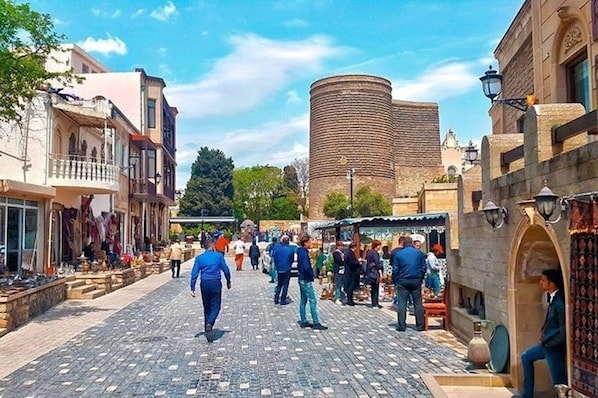 A cobblestone street with shops and a large cylindrical tower in the background. -  Retro Silent Boutique Hotel (Baku)