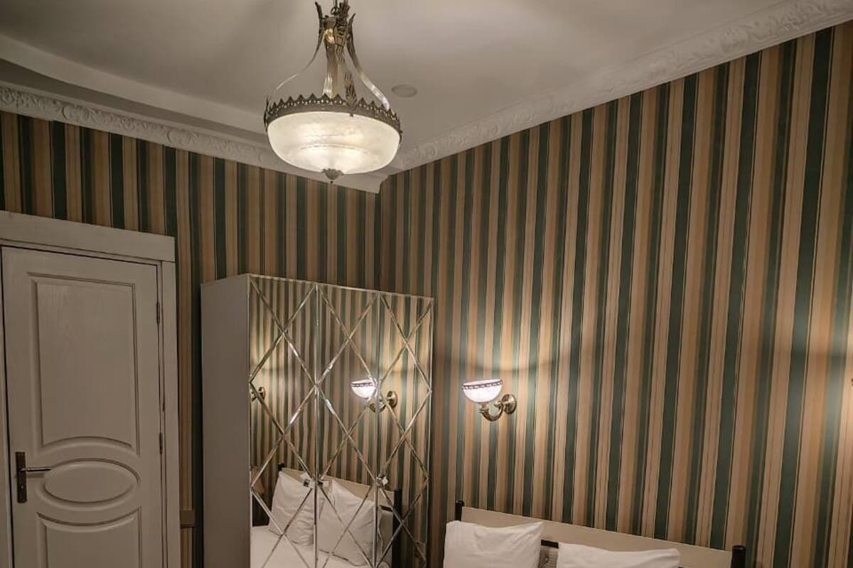 A hotel room with two beds, a wardrobe, a chandelier, and striped wallpaper.