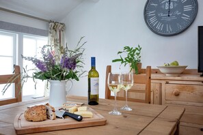 Een houten tafel met een snijplank, kaas, brood, een fles wijn en twee glazen witte wijn.
