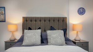 Quarto com cabeceira estofada, duas luminárias de apoio e almofadas decorativas com estampas de elefantes.