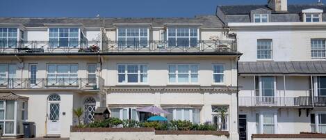 A row of terraced houses with balconies, a clear sky, and a street in front.